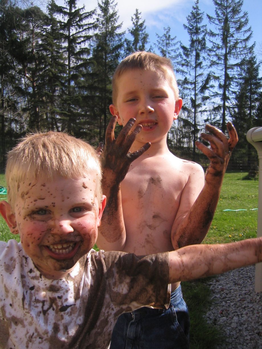 Kevin and Alex as small boys, covered head to toe in mud, grinning at the camera in the back yard